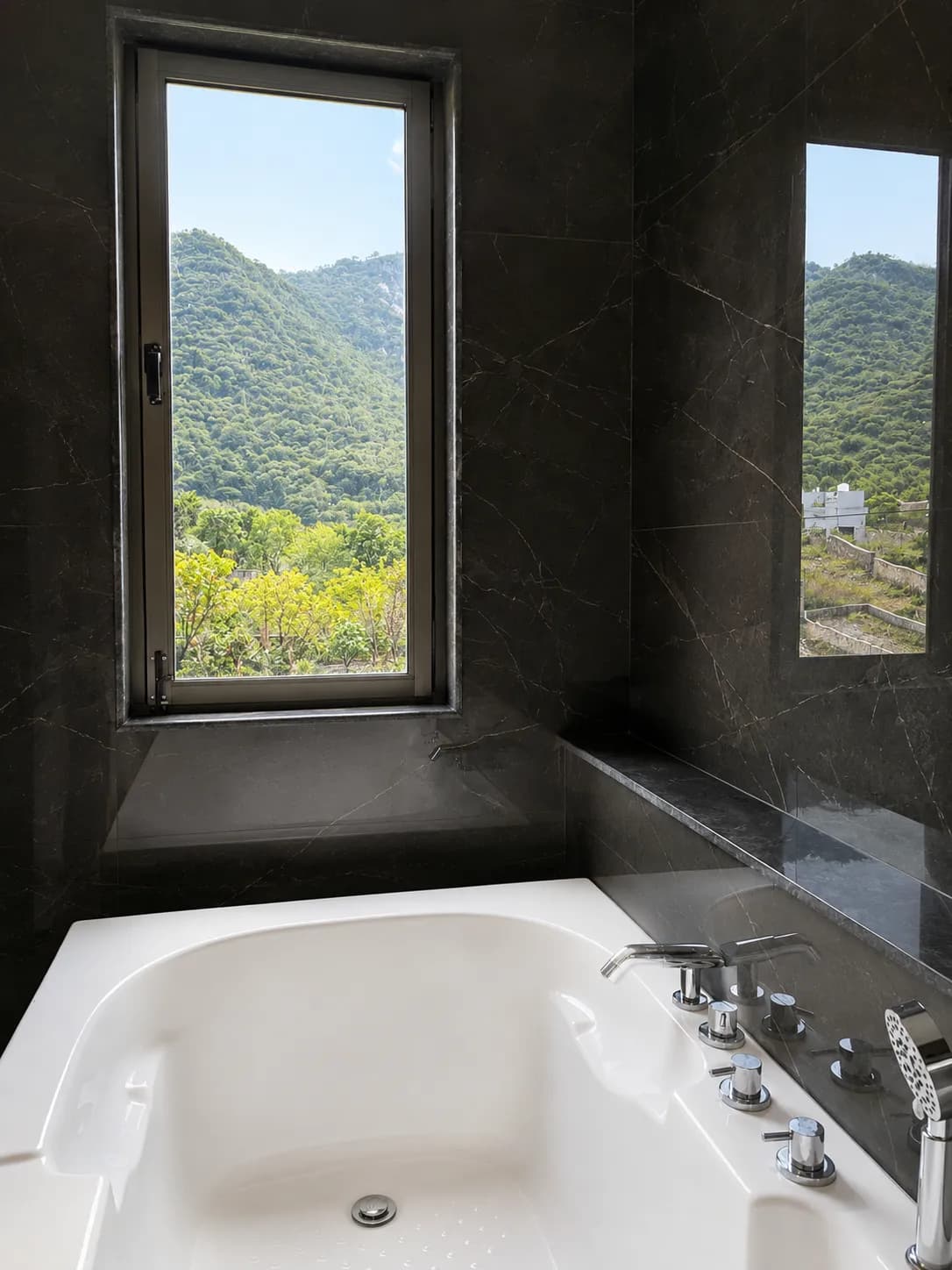 Deep soaking bathtub in dark marble with a window framing the green Aravalli Hills